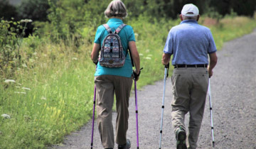 Älteres Paar beim Nordic Walking auf einem Naturweg, gemeinsam aktiv unterwegs in grüner Landschaft als Symbol für aktives Altern und Bewegung im Alltag