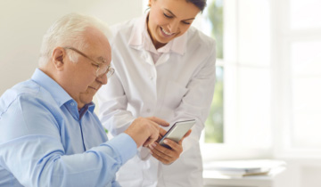 Pflegerin halt einem Patientin ihr Smartphone hin, um ihm eine Pflege-App zu zeigen
