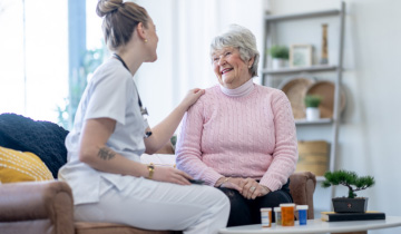 Eine junge Pflegerin und eine ältere Patientin sitzen zusammen auf der Couch und verstehen sich gut