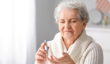 Eine ältere Dame im weißen Pullover ermittelt mit einem kleinen medizinischen Gerät ihren Blutzuckerwert, um der Diabetes vorzubeugen