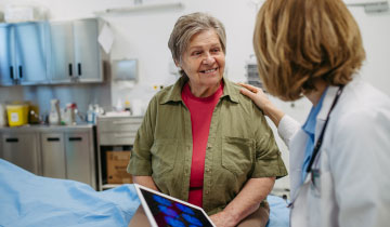 Ärztin im freundlichen Gespräch mit älterer Patientin während eines Gesundheitschecks im Behandlungszimmer