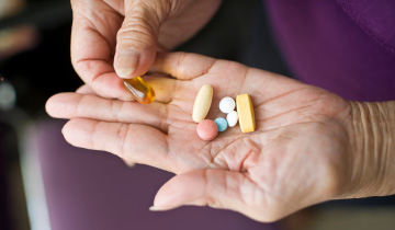 Auf der Hand eines älteren Menschen liegen diverse Mediakante und Kapsel- und Tablettenform, die die Person betrachtet