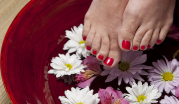 Fußbad mit roten lackierten Zehen und Blüten in einer roten Schale als Sinnbild für mobile Fußpflege oder Wellness