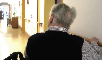 �lterer Mann schaut im Rollstuhl sitzend einen Flur entlang, aufgenommen von hinten, Symbol f�r Pflege, Alter und Selbstst�ndigkeit.