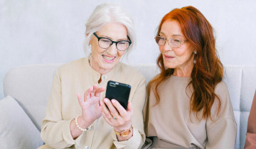 Zwei junggebliebene, fröhliche Seniorinnen beschäftigen sich mit einem Smartphone in den sozialen Medien