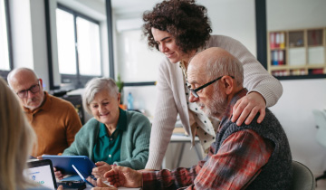 Ältere Menschen lernen gemeinsam mit einer jüngeren Betreuungsperson den Umgang mit Tablet und Smartphone in einer freundlichen Schulungssituation