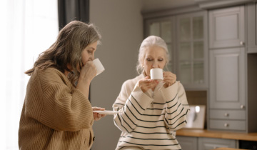 Zwei ältere Damen sitzen an einem Küchentresen und trinken etwas aus Bechern