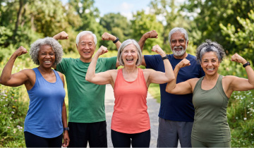 Aktive Seniorinnen und Senioren stehen lächelnd im Park und zeigen ihre Muskeln als Symbol für gesundes Altern, Fitness und Lebensfreude.