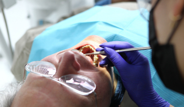 Ein Senior liegt auf einem Zahnarztstuhl und wird mit weit geöffnetem Mund behandelt.