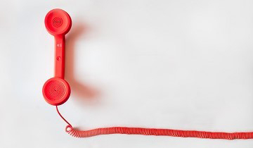 Roter Telefonhörer mit Schnur auf weißem Grund