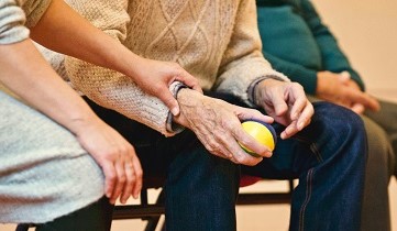 Frau hält Hand einer älteren Person, die einen kleinen Ball hält.