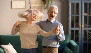 Zwei ältere Menschen tanzen fröhlich im Wohnzimmer