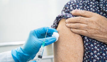 Eine Kanüle wird am Arm einer Seniorin angesetzt, um sie zu impfen